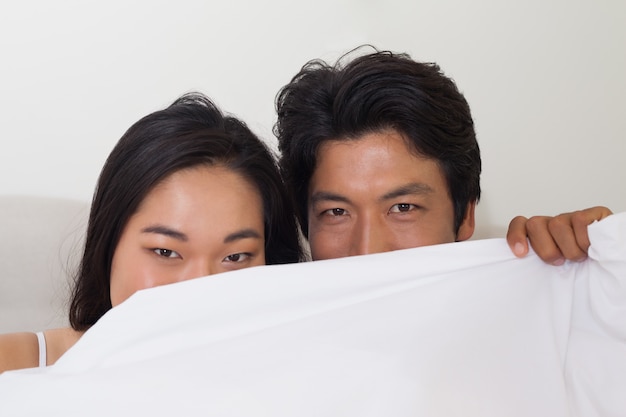 Happy couple holding duvet over face