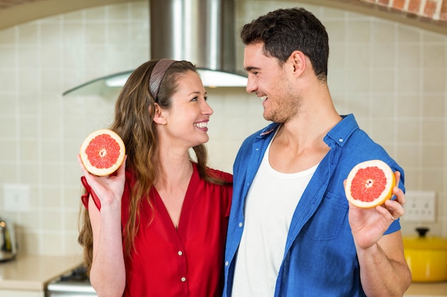 Happy couple holding slices of blood orange in kitchen