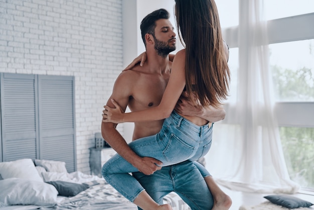 Happy couple at home. Beautiful young couple embracing while standing in the bedroom