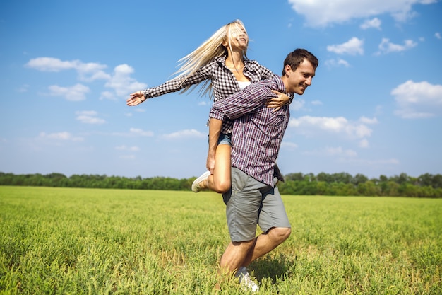 Happy couple is running together in green field while holding red balloons