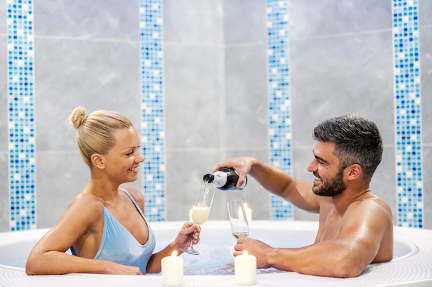 A happy couple is sitting in a hot tub surrounded by candles and enjoying romantic moments