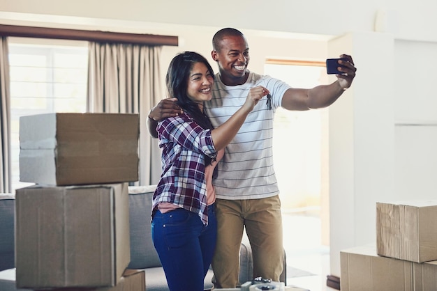 Happy couple keys and selfie in new home for moving real estate and property investment with box People memory and rent in house for mortgage success social media or milestone with loan approval