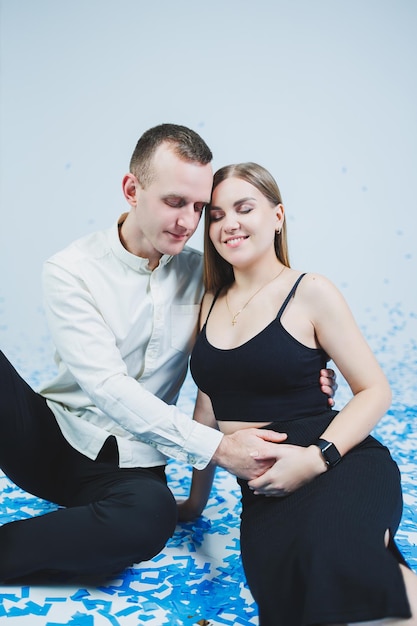 Happy couple laughing at gender party while sitting in blue confetti Gender party