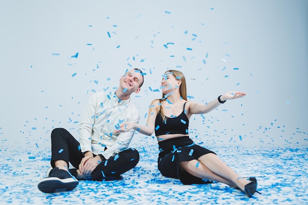 Happy couple laughing at gender party while sitting in blue confetti Gender party