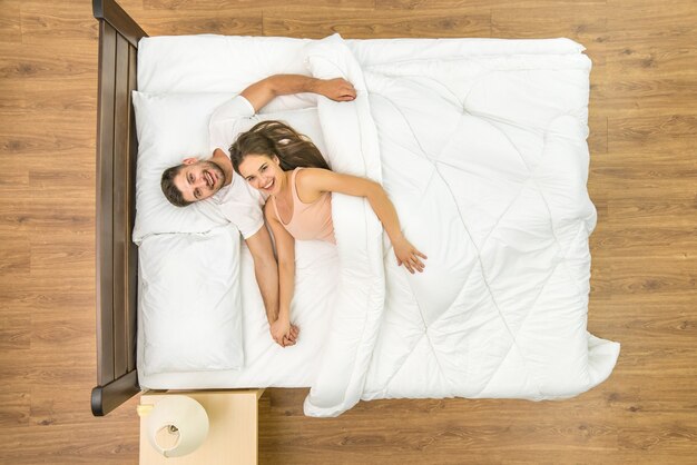 The happy couple look to the camera on the bed. View from above