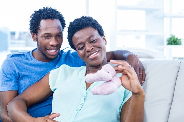 Happy couple looking at baby shoes while sitting on sofa at home