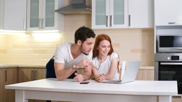 happy couple looking at laptop at home in the kitchen