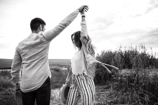 Happy couple in love hugging, kissing and smiling against the sky in field. Hat in girl's hand