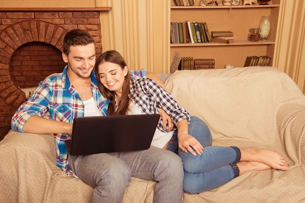 Счастливая влюбленная пара с ноутбуком, сидя на диване