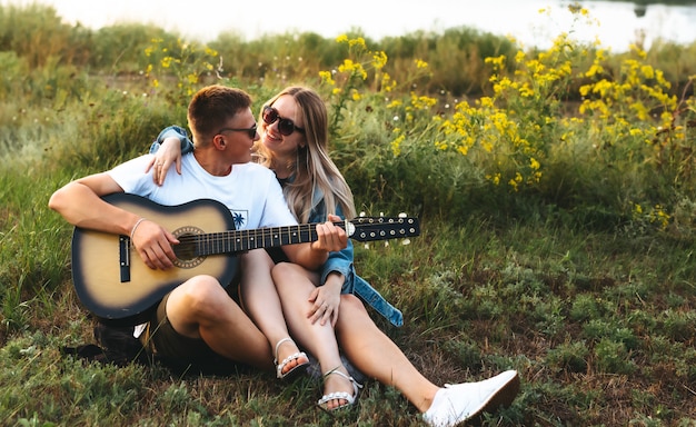 A happy couple in love with sunglasses playing the guitar and rejoicing at sunset.