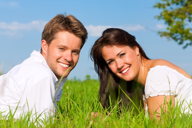 日当たりの良い牧草地で草で横になっている幸せなカップル