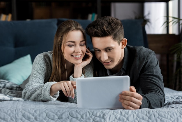 happy couple lying and looking at tablet