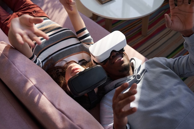 Happy couple lying on sofa and having fun with new trends technology