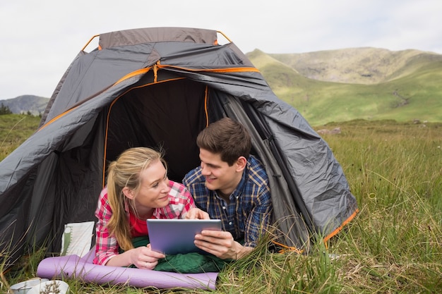 Счастливая пара, лежащих в их палатке и используя цифровой планшет