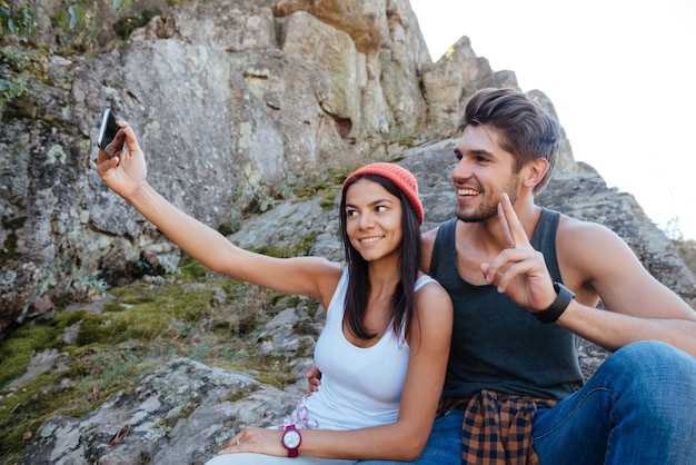 Le coppie felici fanno selfie e si siedono sulla roccia. ragazza che tiene il telefono