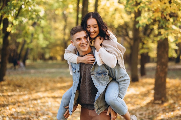 背中の後ろに女性を抱き、秋の公園で一緒に楽しんでいる幸せなカップルの男