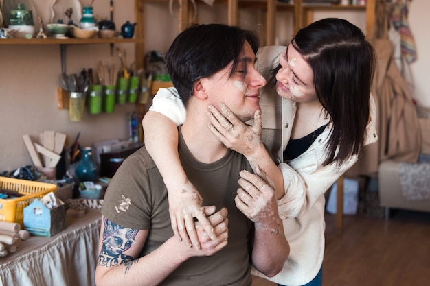 Happy couple man and woman dirty face in pottery studio, dating in ceramics workshop