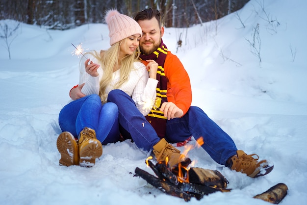 Happy couple man and woman hugging in winter in the forest by the fire with sparklers