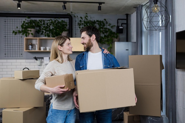 Happy couple man and woman live together moved to a new rented apartment holding cardboard boxes