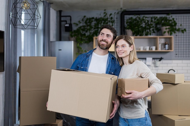 Happy couple man and woman live together moved to a new rented apartment holding cardboard boxes