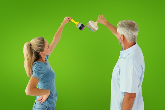 Happy couple painting wall with paintbrushes against green vignette