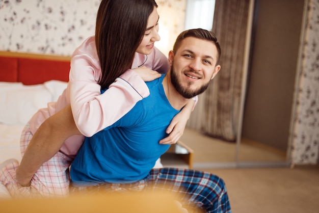 Happy couple in pajamas relaxing in bed at home, good morning. Harmonious relationship in young family. Man and woman resting together in their house, carefree weekend