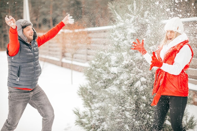 冬休みに雪遊びをする幸せなカップル、人々は楽しんでいます。女性と男性は週末にモミの木の近くでユーモアの瞬間を持っています