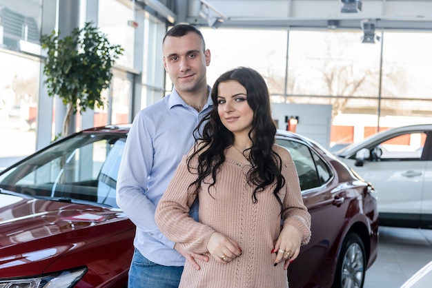 Happy couple posing with new cars in showroom