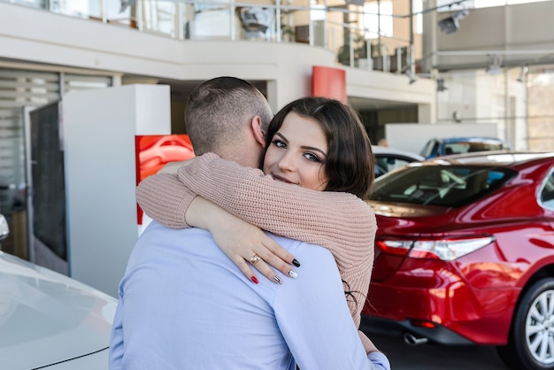 Happy couple posing with new cars in showroom