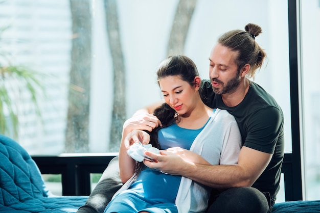 Happy couple pregnant woman and husband stay home in living room Happy couple taking care together