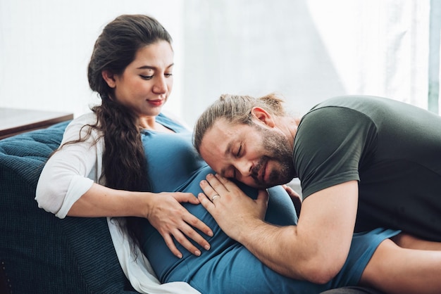 Happy couple pregnant woman and husband stay home in living room Happy couple taking care together