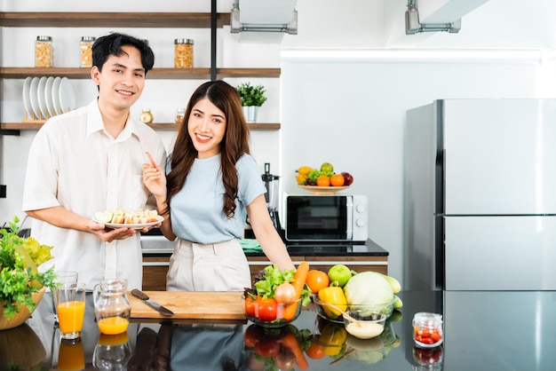 A happy couple prepares and cooks healthy salad with vegetables on a cutting board together in the home kitchen Food cooking for young couple husband and wife in a good mood and healthy relationship