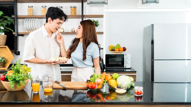 幸せな夫婦が家庭の台所で一緒にまな板の上で野菜を使った健康的なサラダを準備して料理する
