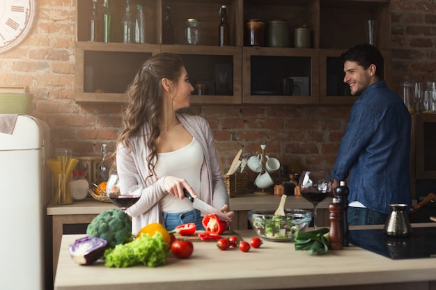 Happy couple preparing dinner together in their loft kitchen at home. Making vegetable salad.
