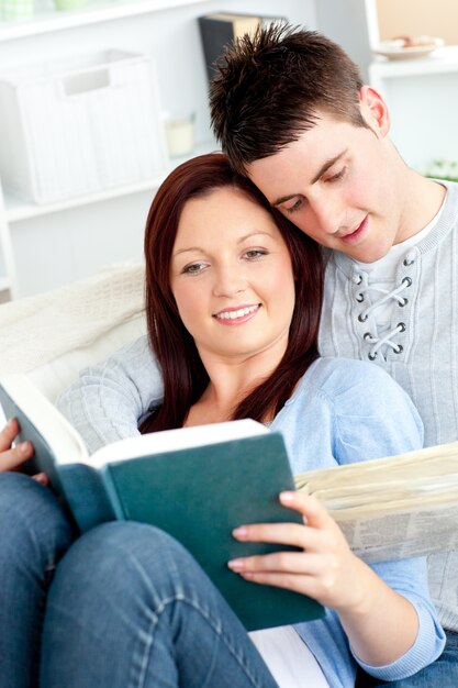 Happy couple reading a book in the living-room lying on the sofa