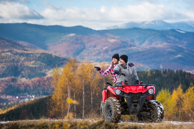 Happy couple on red quad bike riding in the mountains. 