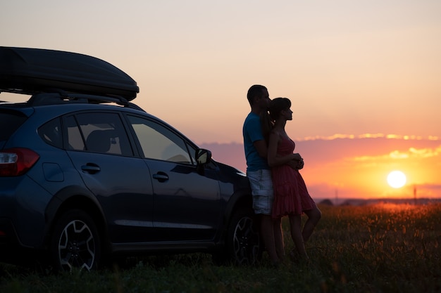 Coppia felice rilassante accanto alla loro auto suv durante il viaggio di luna di miele al tramonto. giovane e donna che si godono il tempo insieme viaggiando in veicolo.