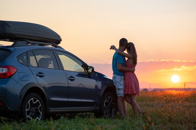 Photo happy couple relaxing beside their suv car during honeymoon road trip at sunset.