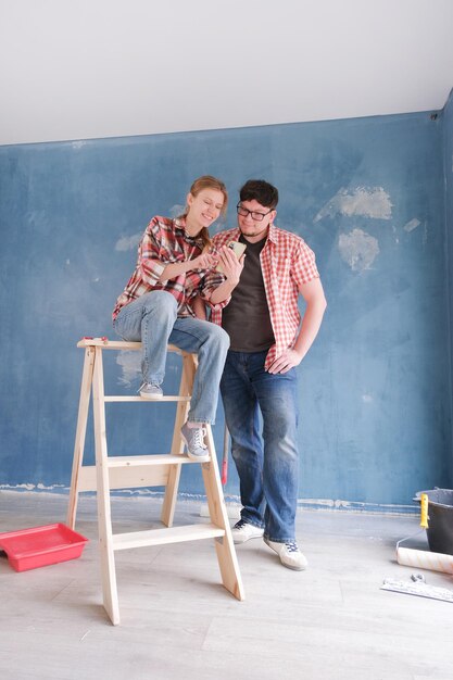 happy couple renovating new house apartment looking to the smartphone family man woman repair flat themselves