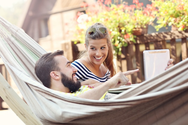 happy couple resting on hammock with tablet