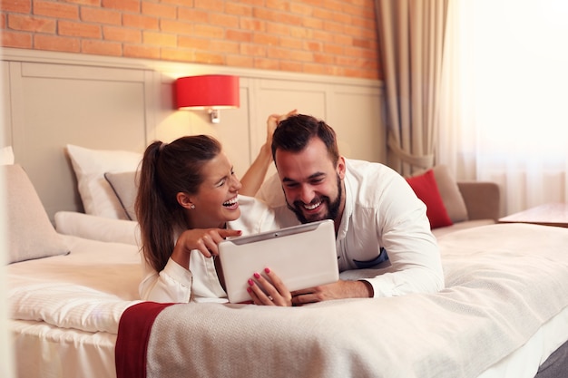 Happy couple resting in hotel room and using tablet