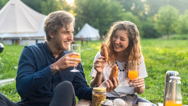 グランピングで自然の中で休んでいる幸せなカップル。飲み物や食べ物、周りの緑