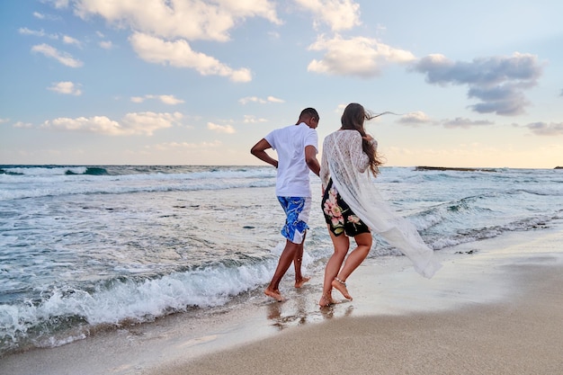 Happy couple running together on beach on summer day back view