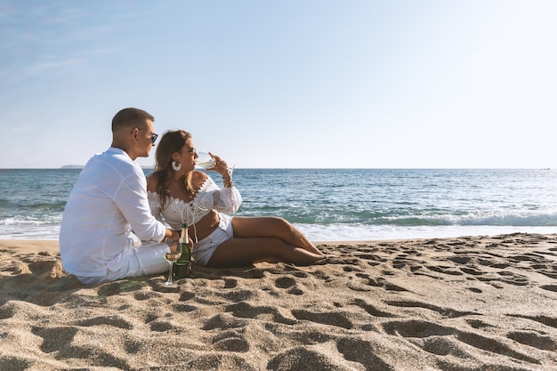 Happy couple seating with champagne on the beach.