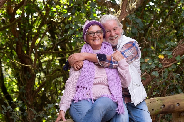 An happy couple of senior man and woman enjoying mountain excursion in the woods at fall season embracing and smiling looking at camera active retired elderly and fun concept