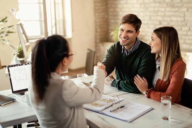 Happy couple shaking hands with insurance agent on a meeting in the office Focus is on man