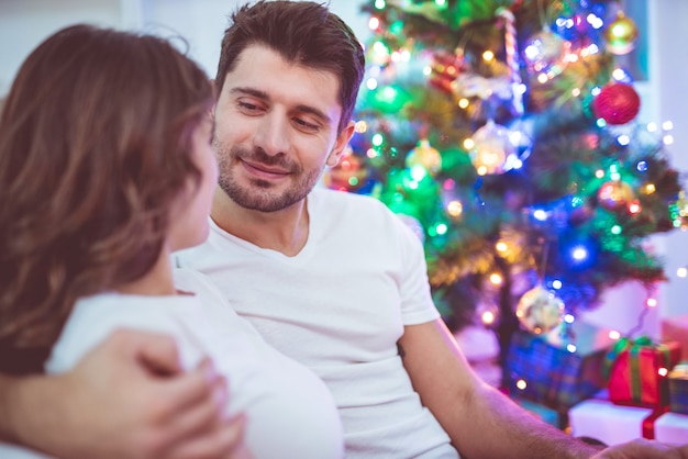 행복한 커플은 크리스마스 트리 근처에 앉아서 포옹한다