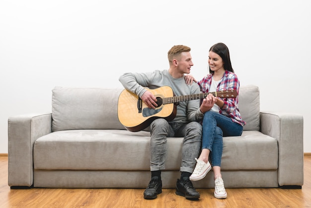 The happy couple sit on a sofa and play the guitar on the white wall background