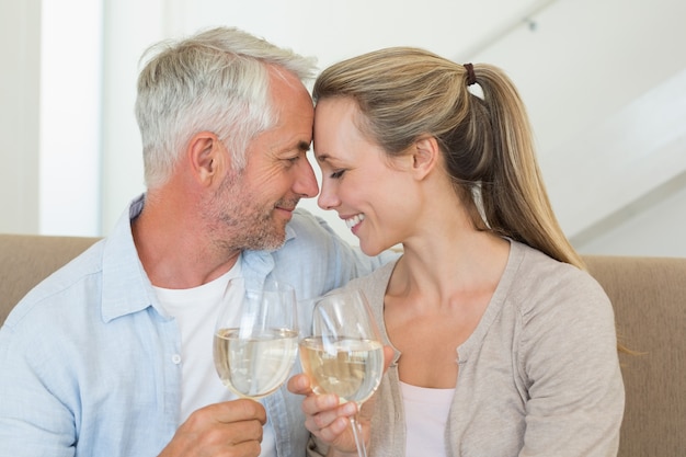 Happy couple sitting on couch toasting with white wine