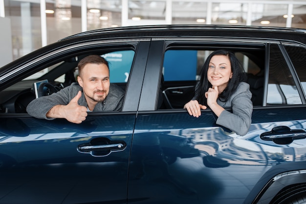 Happy couple sitting in new car, showroom.